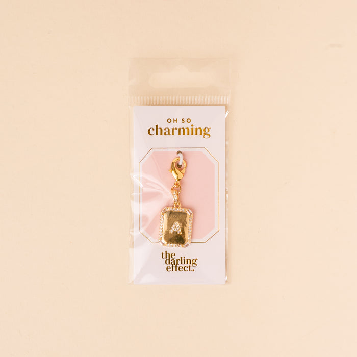 The-darling-effect’s A Jewelry Charm Initial Letter Gold features a gold-plated letter and clasp, attached to an “OH SO charming and the darling effect” card, all in a clear pouch—a perfect personalized jewelry piece.