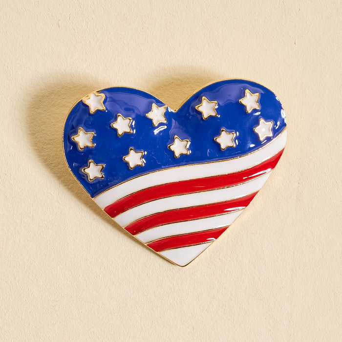 The Darling Effect's Americana Heart Timeless Brooch features a vintage-inspired heart design with blue and white stars above red and white stripes, styled like the American flag against a plain beige background.