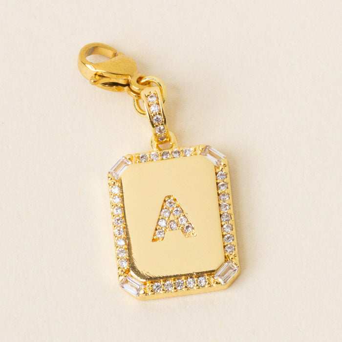 The-darling-effect’s A Jewelry Charm Initial Letter Gold features a gold-plated rectangular pendant with a diamond border and raised letter A, attached to a matching clasp—perfect for adding personalized style to your jewelry collection.
