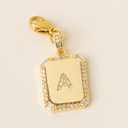 The-darling-effect’s A Jewelry Charm Initial Letter Gold features a gold-plated rectangular pendant with a diamond border and raised letter A, attached to a matching clasp—perfect for adding personalized style to your jewelry collection.