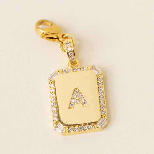 The-darling-effect’s A Jewelry Charm Initial Letter Gold features a gold-plated rectangular pendant with a diamond border and raised letter A, attached to a matching clasp—perfect for adding personalized style to your jewelry collection.