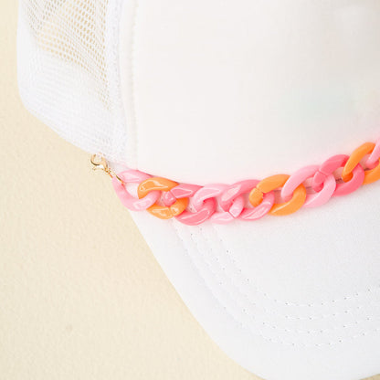 Close-up of The Darling Effect's Acrylic Sassy Trucker Hat Chain, featuring a white mesh trucker cap with a chunky pink and orange plastic chain along the brim. Shown against a simple light background.