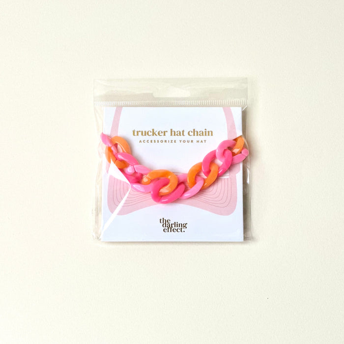 The Darling Effect’s Acrylic Sassy Trucker Hat Chain in pink and orange is a fun hat accessory, packaged on a white card with a pink hat illustration and “Accessorize your hat.”.
