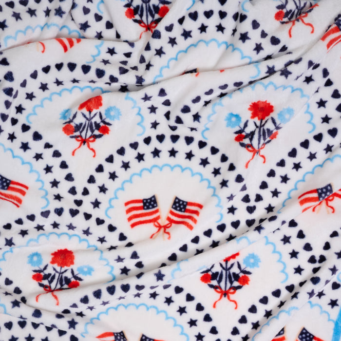 The Darling Effect's All-American Darling Snuggle Up Plush Blanket features white fleece with American flags, florals, stars, hearts, and medallion borders—a cozy throw for timeless patriotic style.