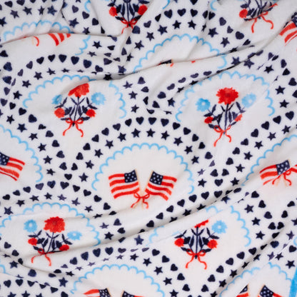 The Darling Effect's All-American Darling Snuggle Up Plush Blanket features white fleece with American flags, florals, stars, hearts, and medallion borders—a cozy throw for timeless patriotic style.