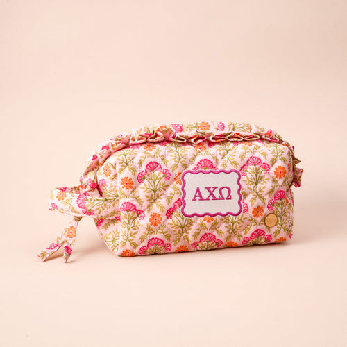 The Darling Effect Alpha Chi Omega Essentials Quilted Cosmetic Pouch features a cream background with pink and orange floral print, a knot handle, and a pink ΑΧΩ patch—the perfect sorority cosmetic pouch.