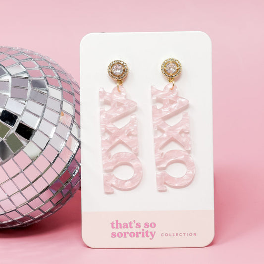 Alpha Chi Omega Letter Pink Acrylic Earrings by The Darling Effect are shown on a white "that's so sorority collection" card, beside a silver disco ball on a pink background—perfect for sisterhood events or bid-day baskets.