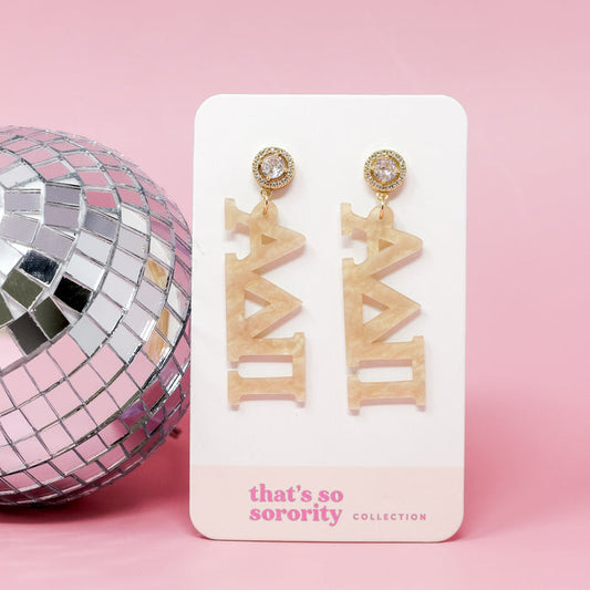 Alpha Delta Pi Sorority Letter Gold Acrylic Earrings by The Darling Effect, shown on a white card beside a disco ball with a pink background—great for sisterhood events or adding sparkle to your bid-day basket.