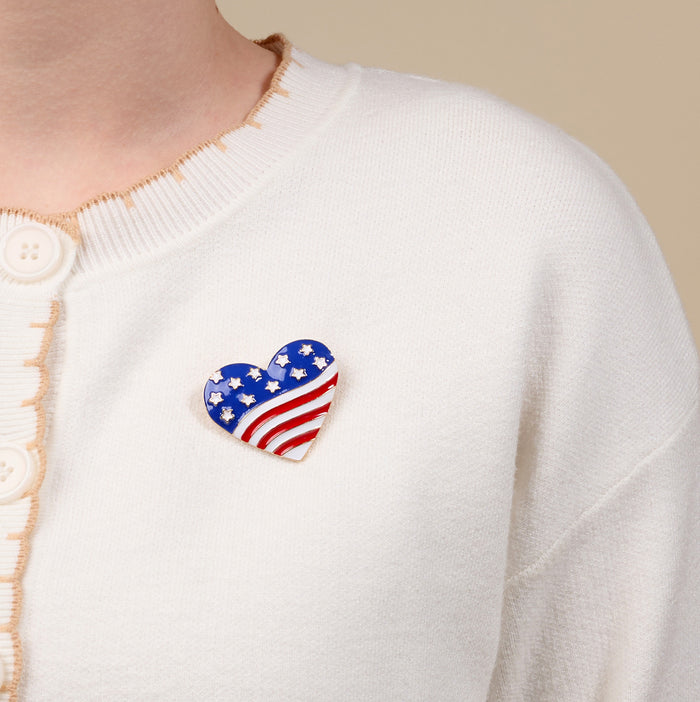 The Darling Effect’s Americana Heart Timeless Brooch, elegantly styled, is worn on a cream-colored cardigan.