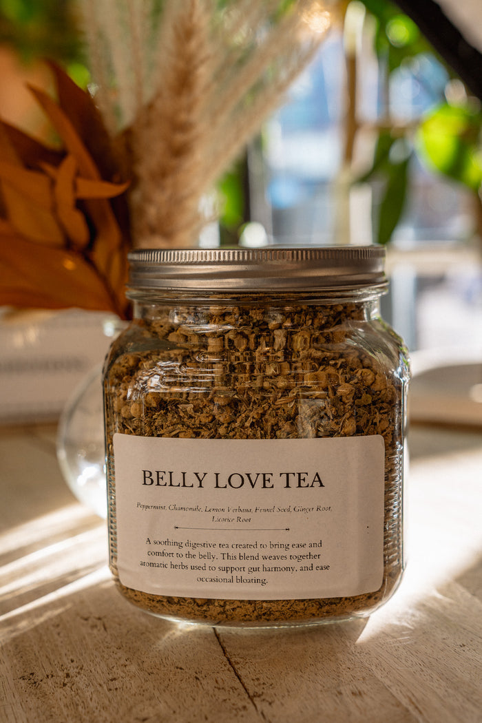 Jar of 'Belly Love Tea' on a wooden surface with blurred background