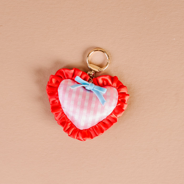 The Darling Effect's Berry Sweet Puffy Heart Bag Charm features pink and white checkers, a blue bow, red ruffled trim, and a gold ring—perfect for adding cute flair to any bag.