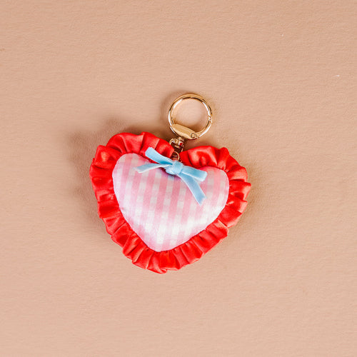 The Darling Effect's Berry Sweet Puffy Heart Bag Charm features pink and white checkers, a blue bow, red ruffled trim, and a gold ring—perfect for adding cute flair to any bag.