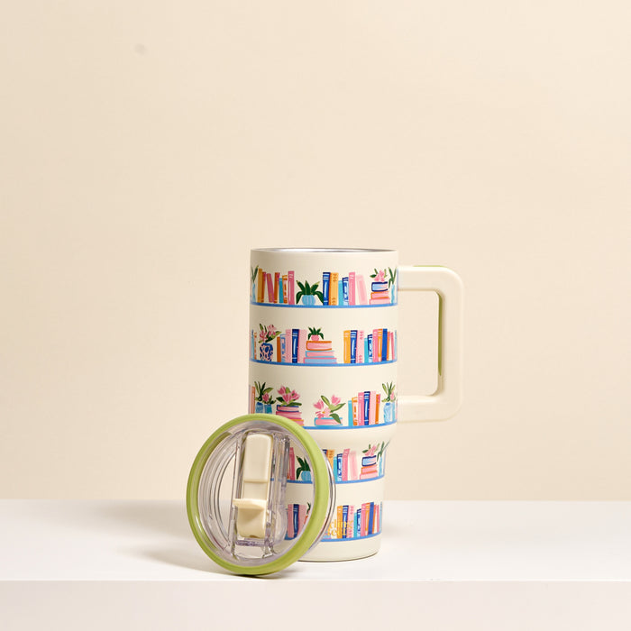 The Darling Effect Book Shelfie 20 oz Lifestyle Flip Straw Tumbler features a cream finish with a bookshelf design of colorful books and plants. This insulated stainless steel tumbler includes a clear lid with a green rim to keep drinks at the ideal temperature.