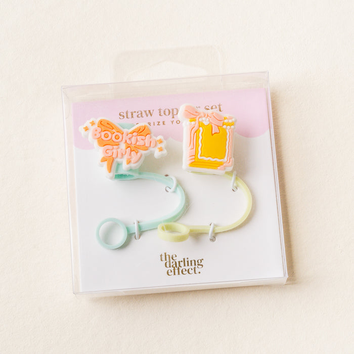 The Bookish Girly Straw Topper Set by the-darling-effect includes two pastel silicone toppers—one as an open book and one with "Bookish Girl" text. Leak-resistant drinkware accessories; packaging features The Darling Effect branding.