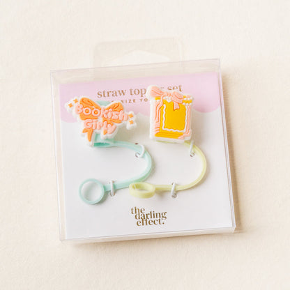 The Bookish Girly Straw Topper Set by the-darling-effect includes two pastel silicone toppers—one as an open book and one with "Bookish Girl" text. Leak-resistant drinkware accessories; packaging features The Darling Effect branding.