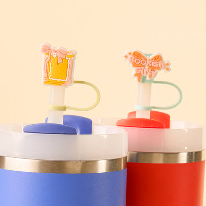The Bookish Girly Straw Topper Set by the-darling-effect features two colorful tumblers: a blue cup with a yellow frame and pink bow on its leak-resistant lid, and a red cup with a "Bookish Girly" topper accented by stars.