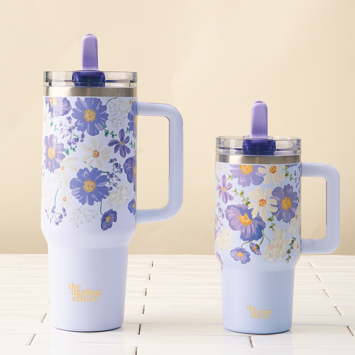 Two Bouquet Beauty Purple 20 oz Lifestyle Flip Straw Tumblers by the-darling-effect, featuring purple floral patterns, handles, leak-resistant clear flip straw lids, and a gold "the darling effect" logo at the base, sit on white tiles.