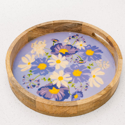 The Bouquet Beauty Purple Large Round Wood Enamel Tray by the-darling-effect features a lavender base with a vibrant floral design in purple, blue, yellow, and white, shown on a white speckled surface.