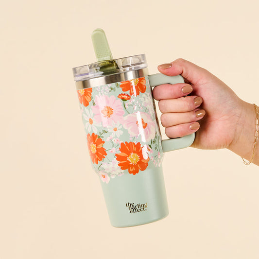 A hand holds the-darling-effect's Bouquet Beauty Sage 20 oz Lifestyle Flip Straw Tumbler, featuring a colorful floral design and a green straw.