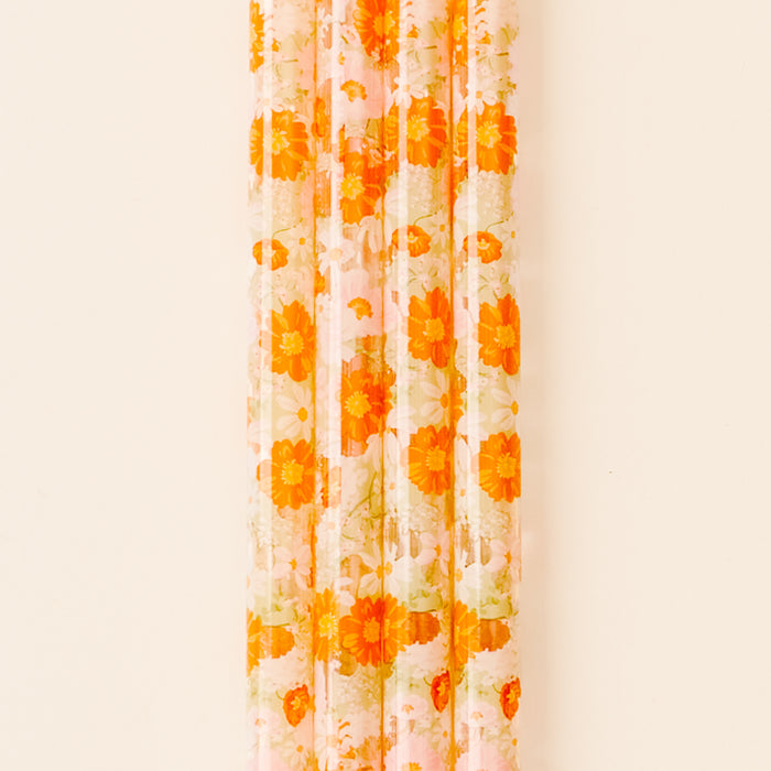 A sheer curtain with an orange and yellow floral pattern hangs against a light wall, while a the-darling-effect Bouquet Beauty Sage 40 oz Tumbler Straw Set adds a pop of color to the scene.