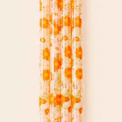 A sheer curtain with an orange and yellow floral pattern hangs against a light wall, while a the-darling-effect Bouquet Beauty Sage 40 oz Tumbler Straw Set adds a pop of color to the scene.