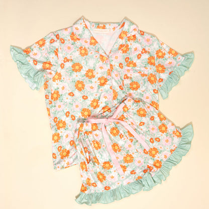The Darling Effect’s Bouquet Beauty Sage Slumber Party Pajama Shorts Set features ultra-soft fabric, a button-up top, floral shorts with sage ruffled edges, and a pink ribbon waist—perfect for lounging or gifting.