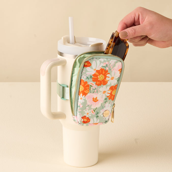 A hand puts sunglasses into the Bouquet Beauty Sage Tumbler Fanny Pack by the-darling-effect, a water resistant, floral pouch attached to a large white tumbler with handle for hands-free convenience.