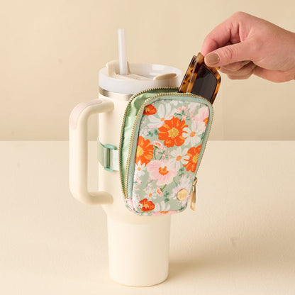 A hand puts sunglasses into the Bouquet Beauty Sage Tumbler Fanny Pack by the-darling-effect, a water resistant, floral pouch attached to a large white tumbler with handle for hands-free convenience.