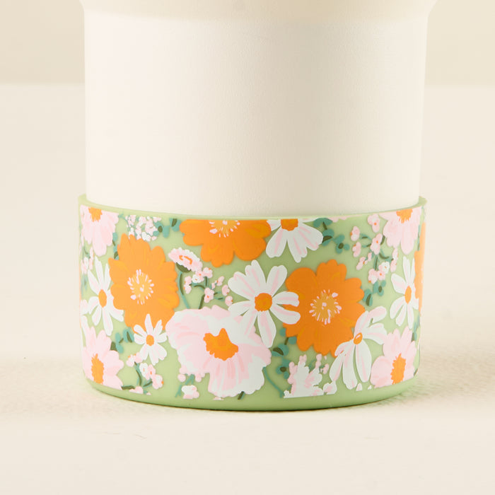 The-darling-effect’s Bouquet Beauty Sage Tumbler Silicone Boot features a light-colored cylindrical tumbler with a green silicone boot and a retro floral pattern of orange, pink, and white flowers for added protection against dents.
