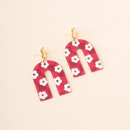 The Darling Effect's Burgundy Game Day Acrylic Earrings feature arch-shaped burgundy acrylic with white flowers and gold hooks, displayed on a light beige background.