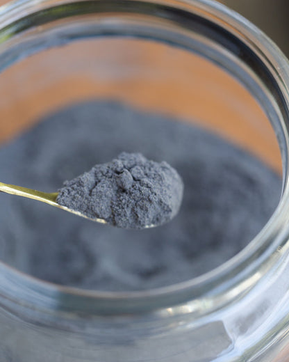 Spoonful of dark gray powder over a glass container