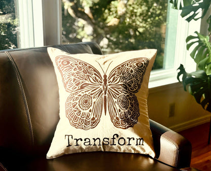 Decorative  20" x 20" natural color cotton canvas pillow with a boho-style brown butterfly design and the word Transform. Handmade by Survivors.