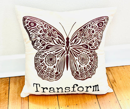 Decorative  20" x 20" natural color cotton canvas pillow with a boho-style brown butterfly design and the word Transform. Handmade by Survivors.