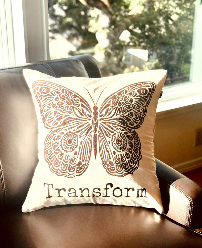 Decorative  20" x 20" natural color cotton canvas pillow with a boho-style brown butterfly design and the word Transform. Handmade by Survivors.
