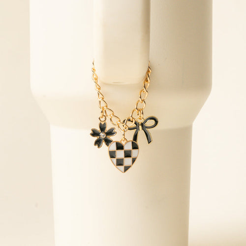 The Checkmate Tumbler Charm by the-darling-effect features a gold chain bracelet with three charms—a black flower, checkered heart, and black bow—ideal as stylish tumbler accessories or unique personalized tumbler charms.