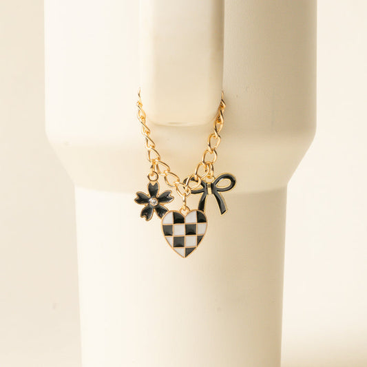 The Checkmate Tumbler Charm by the-darling-effect features a gold chain bracelet with three charms—a black flower, checkered heart, and black bow—ideal as stylish tumbler accessories or unique personalized tumbler charms.