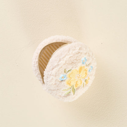The Circle Dainty Floral Yellow Teddy Pouch by the-darling-effect is a round, cream sherpa pouch with yellow and blue floral embroidery and a wipeable lining, shown on a light beige background.