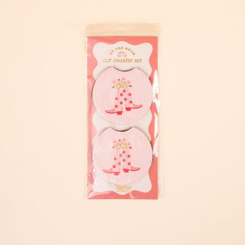The Darling Effect’s Cowgirl Boots On the Road Car Coaster Set includes two round car coasters with a pink and white striped design, red cowboy boots, and flowers—perfect for adding style to your car cup holder.