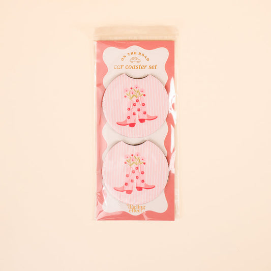The Darling Effect’s Cowgirl Boots On the Road Car Coaster Set includes two round car coasters with a pink and white striped design, red cowboy boots, and flowers—perfect for adding style to your car cup holder.