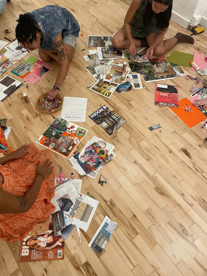 Three people sitting on a wooden floor surrounded by scattered magazines and papers.