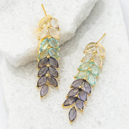 Pair of gold earrings with multicolored stones on a textured white surface
