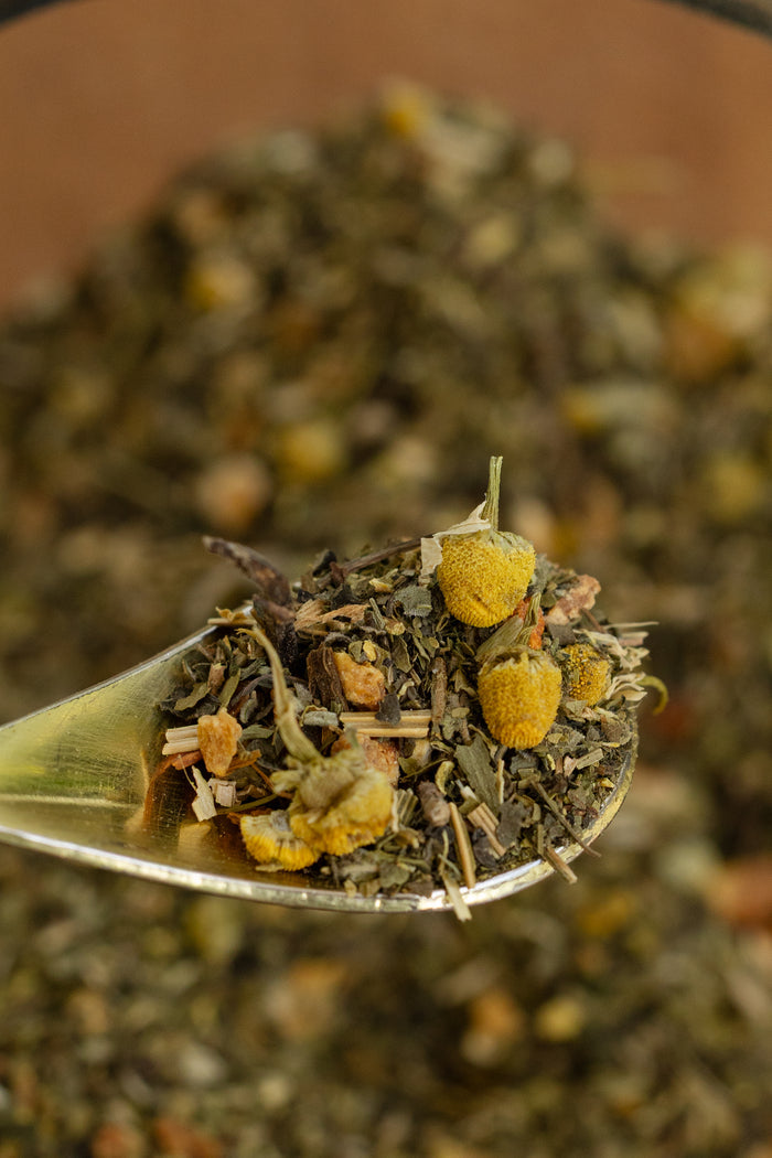 Tea leaves with yellow flowers on a spoon against a blurred tea background