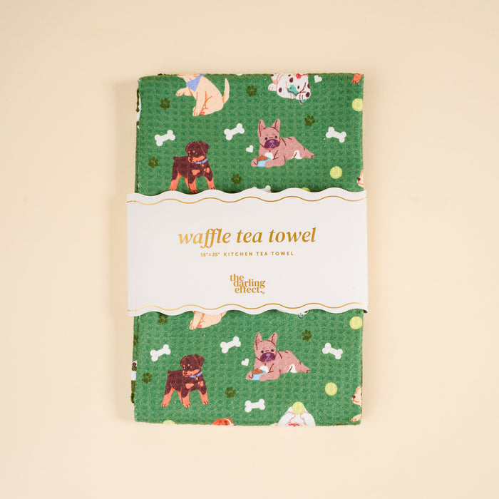 The Dog Days Waffle Tea Towel by The Darling Effect features cartoon dogs and bones, is absorbent and decorative, and comes folded with a label that reads "waffle tea towel" and "The Darling Effect." Great for your kitchen or as a cute home accent.