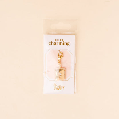The E Jewelry Charm Initial Letter Gold by the-darling-effect features a gold-plated brass book-shaped charm with silver accents and a lobster clasp, presented on a white "OH SO charming" card in clear plastic packaging.