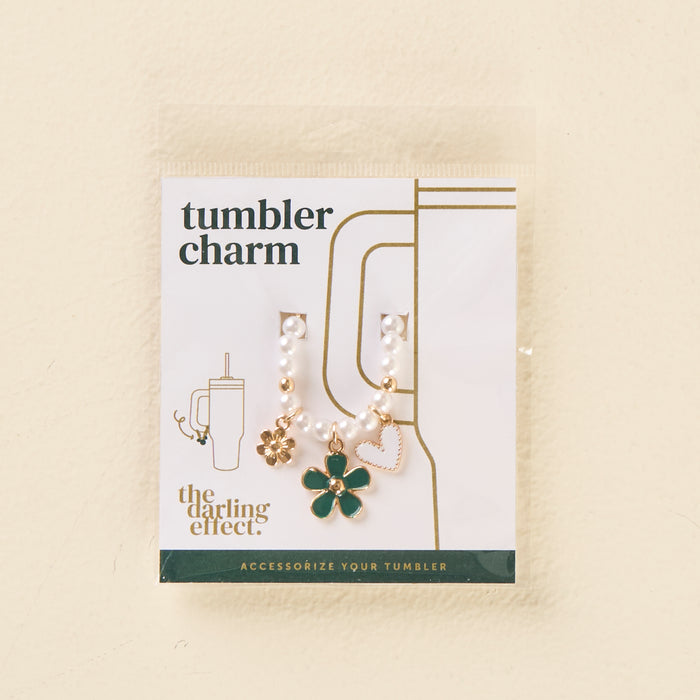 The Enchanted Tumbler Charm by the-darling-effect features a beaded chain with gold and green flower, gold flower, and pink heart charms. The packaging reads "Tumbler Charms" and "the darling effect." Accessorize your tumbler in style!.