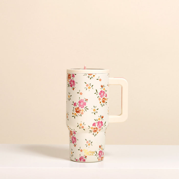 The-darling-effect Endless Daydream Cream 20 oz Lifestyle Flip Straw Tumbler features a pink floral pattern, insulated stainless steel build, and cream handle, shown on a cream background.