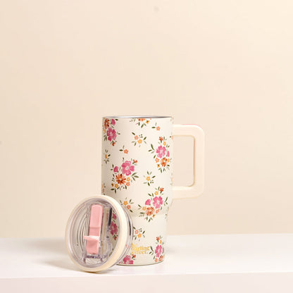 The-darling-effect Endless Daydream Cream 20 oz Lifestyle Flip Straw Tumbler, featuring a pink and orange floral pattern and a pink sliding lid, rests on a white surface with the lid placed beside it.