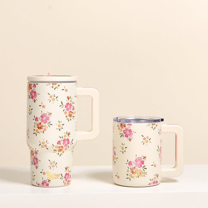 Two cream-colored Endless Daydream 20 oz Lifestyle Flip Straw Tumblers by the-darling-effect, both adorned with pink and green floral patterns, sit side by side on a white surface; the right tumbler is shorter and has a clear lid for extra style.