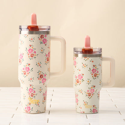 The-darling-effect’s Endless Daydream Cream 40 oz Lifestyle Flip Straw Tumbler and a matching floral tumbler with handles and pink straws sit side by side on a white surface against a beige background.