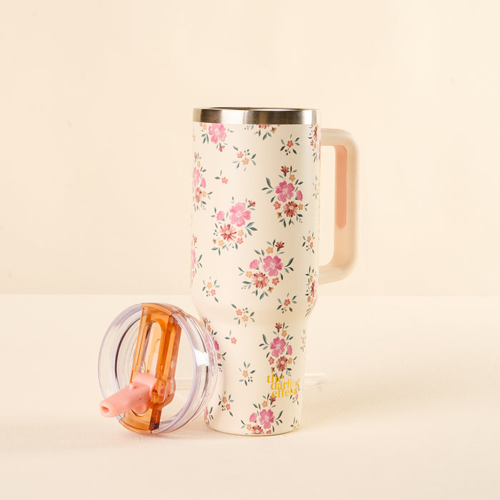 The-darling-effect’s Endless Daydream Cream 40 oz Lifestyle Flip Straw Tumbler features a tall, white body with pink floral patterns, a matching handle, and a transparent lid with an orange slider and pink flip straw for leak-resistance.